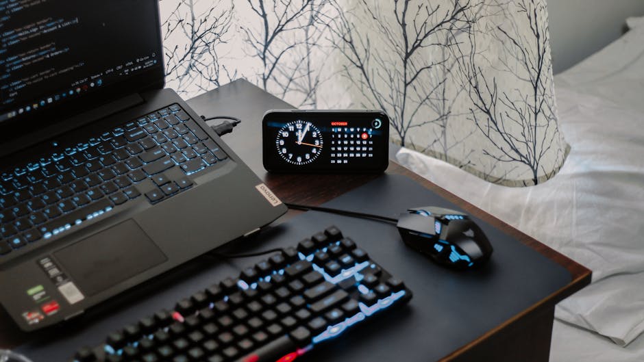 A modern workspace featuring a laptop, digital clock, gaming mouse, and keyboard