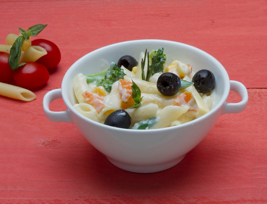 Tasty penne pasta in cream sauce with olives and vegetables on a vibrant background.