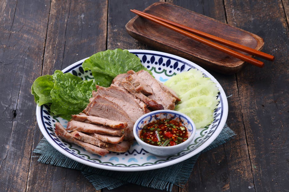 Grilled pork slices with spicy dipping sauce, cucumbers, and lettuce on a decorative plate.