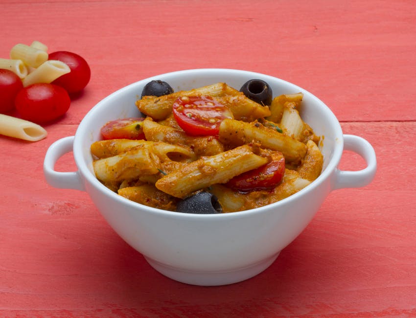 A vibrant bowl of penne pasta with cherry tomatoes and olives served in a white dish.