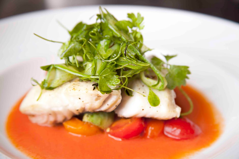 A beautifully presented gourmet fish dish topped with fresh herbs and vibrant vegetables